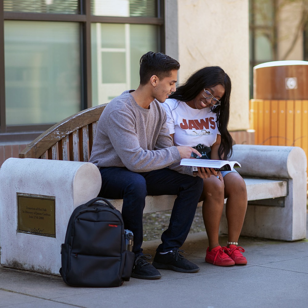male and female students sitting on bench reading textbook